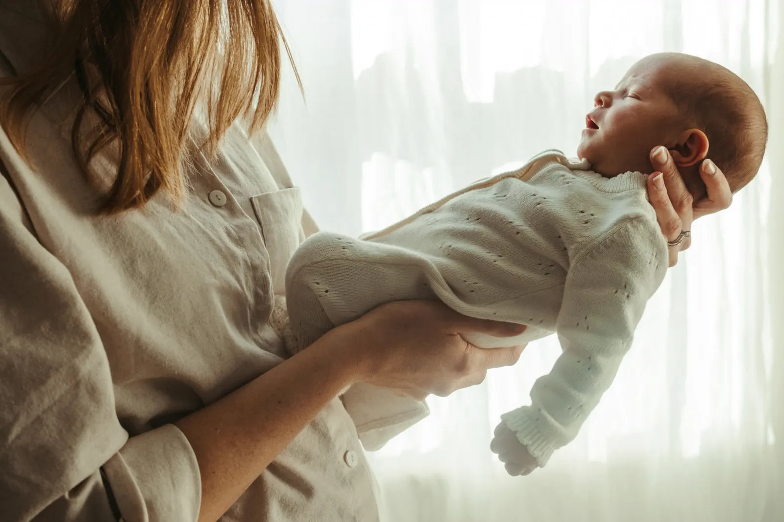 A mother holding her sleeping newborn by a sunlit window