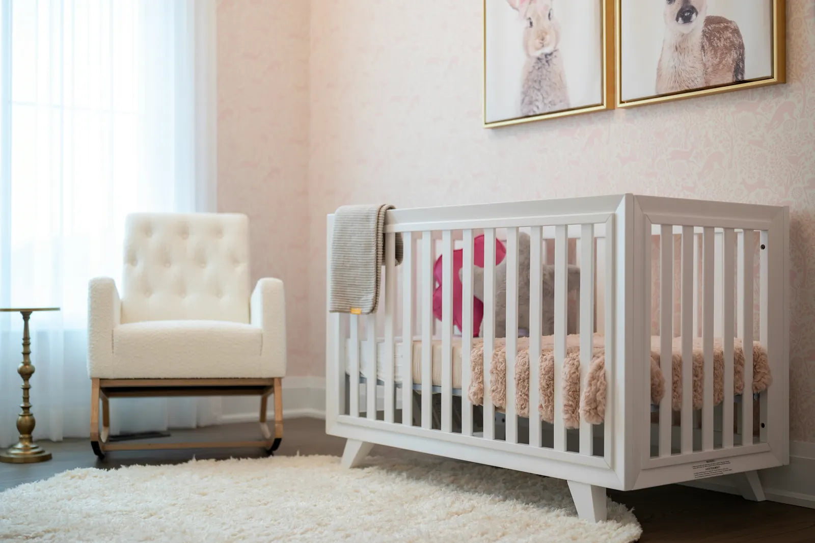 A blush-pink nursery with a white crib and a cream rocking chair